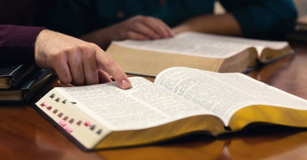 bíblia sobre a mesa e uma pessoa a companhando a leitura